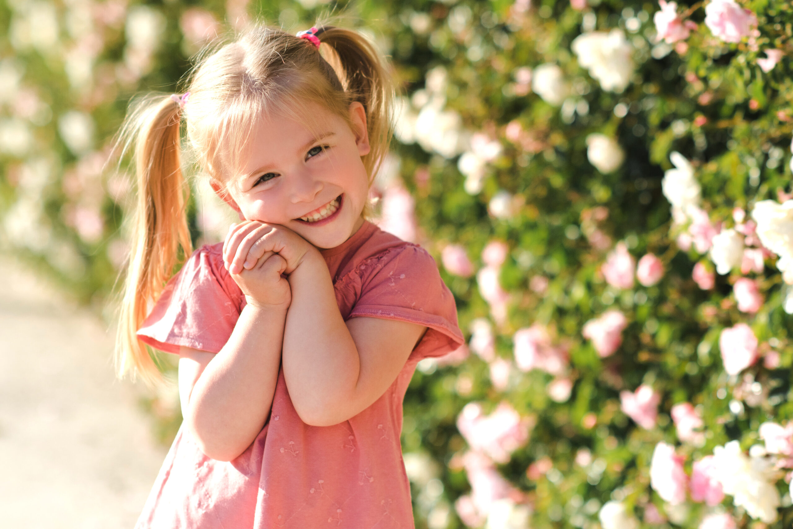 young 5 year old girl posing next to a bush of flowers