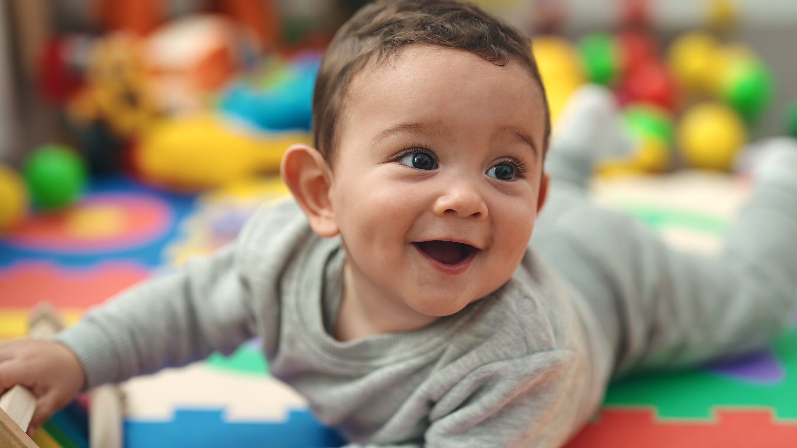 Adorable hispanic baby smiling confident lying on floor at kindergarten